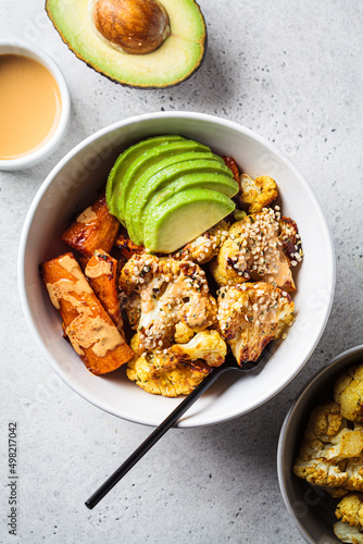 Vegan lunch bowl with baked cauliflower, sweet potato, avocado and peanut butter dressing. Healthy food concept.