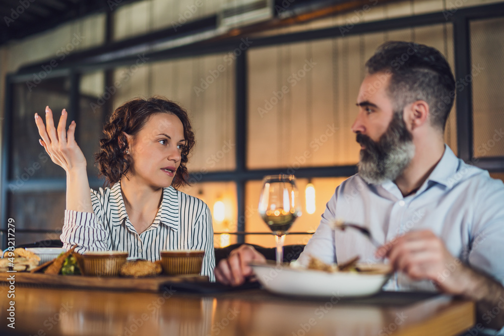 Adult couple is sitting at restaurant. They are having conversation while eating dinner. Adult couple is sitting at restaurant. They are having conversation while eating dinner.