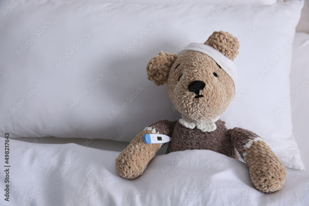 Cute toy bear with bandage and thermometer in bed, space for text. Children's hospital