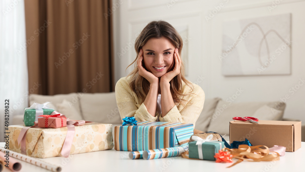 Young woman with beautifully wrapped gifts at table in living room Young woman with beautifully wrapped gifts at table in living room