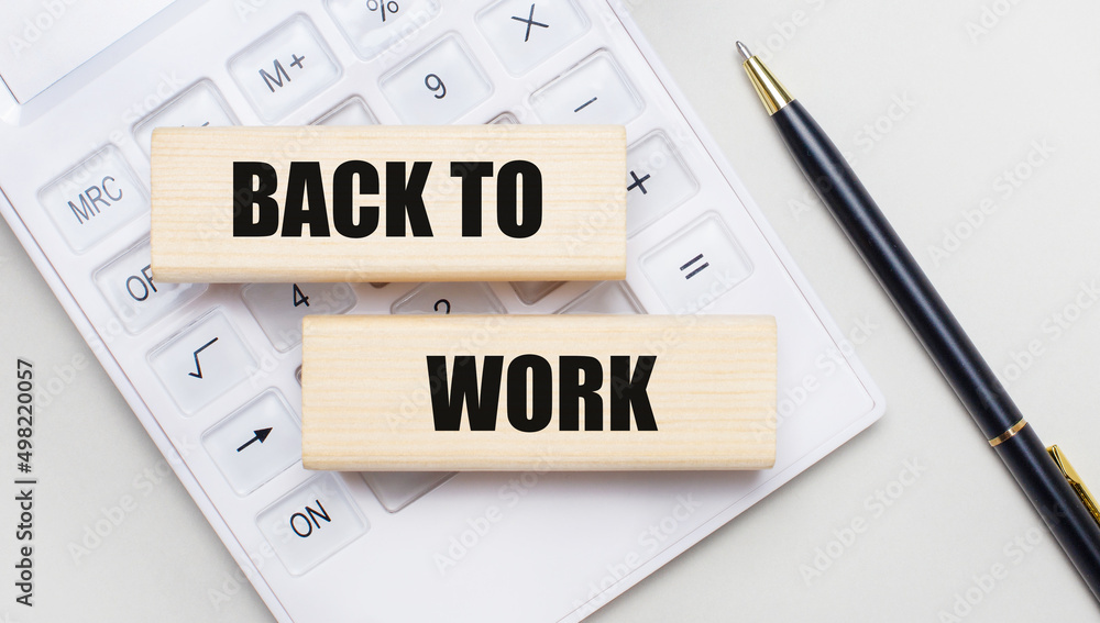 Wooden blocks with the BACK TO WORK Iie on a light background on a white calculator. Nearby is a black handle. Business concept Wooden blocks with the BACK TO WORK Iie on a light background on a white calculator. Nearby is a black handle. Business concept