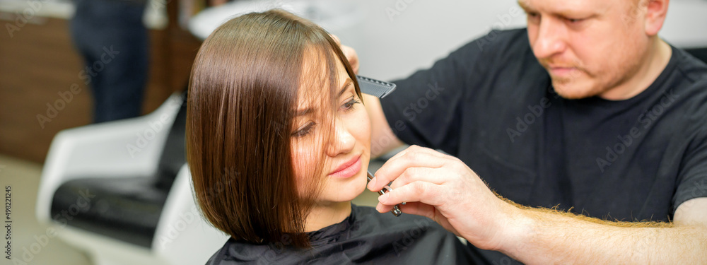 Fototapeta premium Haircut of short hair of young caucasian woman by a male hairdresser in a barbershop