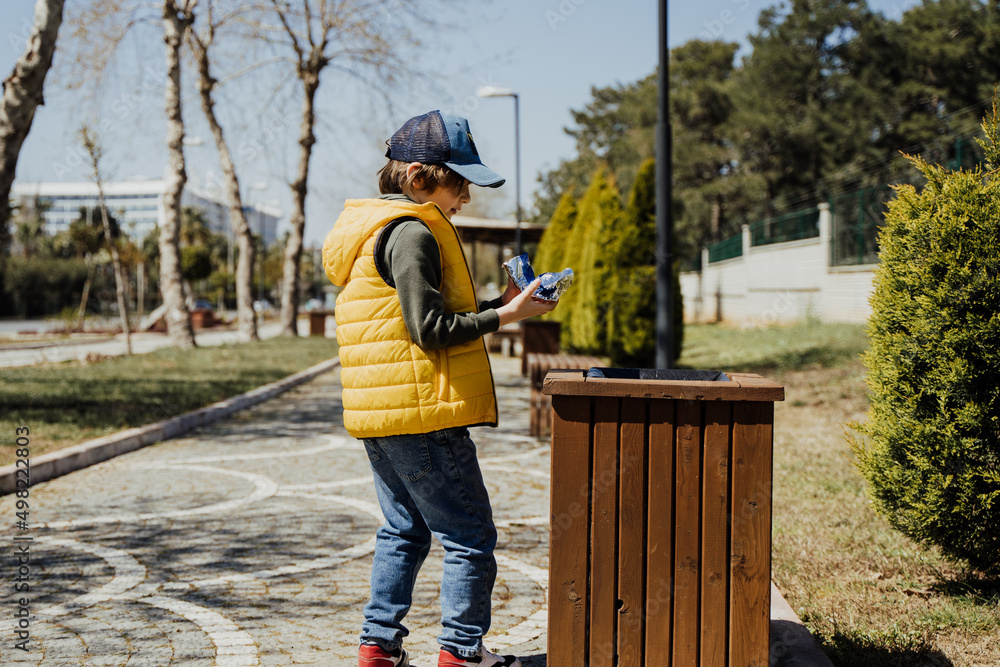 Schoolboy kid throwing the trash into dumpster. Boy using recycling bin