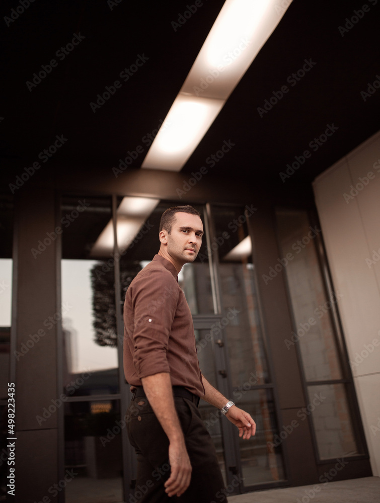 Portrait of a young handsome man with unshaven bristles in a brown shirt on the city street