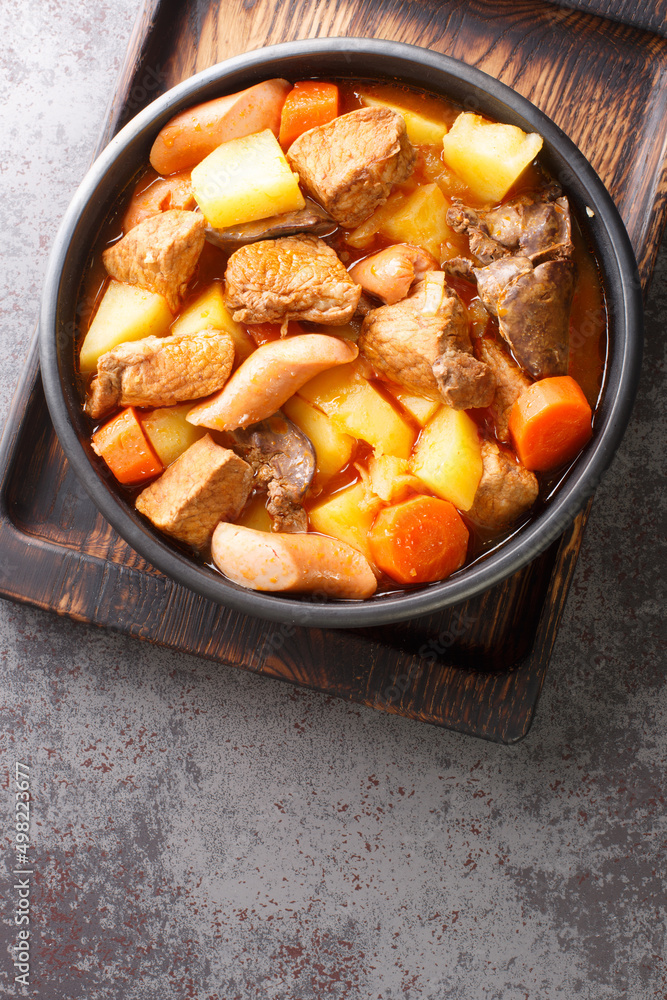 Filipino Menudo is a hearty and tasty pork stew made with fresh tomatoes, potatoes, carrots close up in the plate on the table. Vertical top view from above Filipino Menudo is a hearty and tasty pork stew made with fresh tomatoes, potatoes, carrots close up in the plate on the table. Vertical top view from above