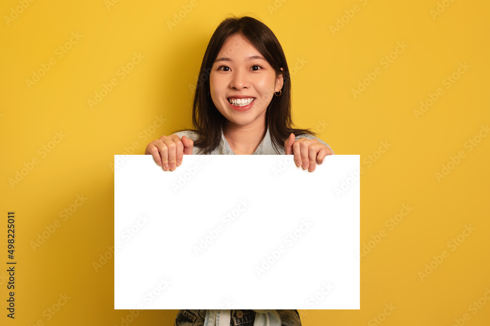 Happy young Asian woman holding blank paper banner, smiling at camera on yellow studio background, mockup Happy young Asian woman holding blank paper banner, smiling at camera on yellow studio background, mockup