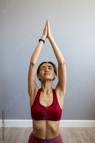 A happy Asian woman sits on a sofa at home and meditates with her wise hands in the lotus position. Smiling young Asian woman relaxes on the couch in the living room, practices yoga