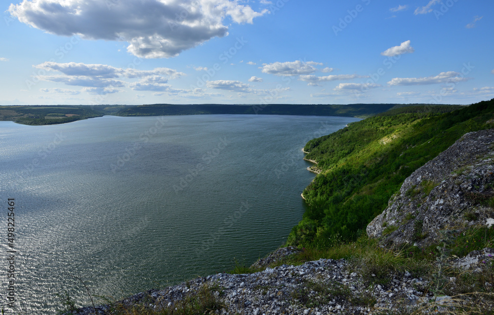 Fototapeta premium The panoramic landscape of Bakota Bay view. Dniester river, Ukraine. The banks of a large river with small waves on the water. Panoramic river, high banks, green hills. Summer day.