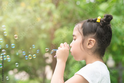 Cute little girl playing  blowing bubble in outdoor summer city park