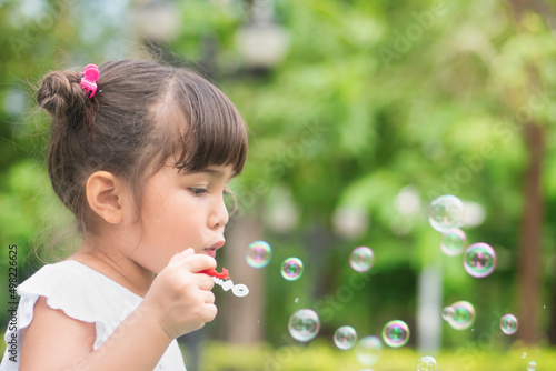Cute little girl playing  blowing bubble in outdoor summer city park