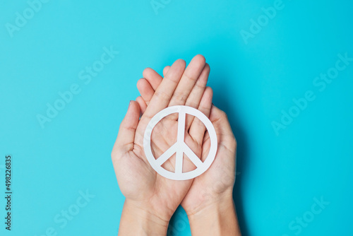 International Day of Peace. Hands holding white paper Peace symbol on blue background. Freedom, Hope, World Peace day 21 September and Nuclear Disarmament concepts.