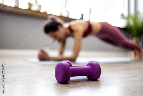An athletic Asian woman standing in an elbow board listens to music on her wireless headphones at home. Side view of an Asian lady exercising her abdominal muscles. Training in the living room. 