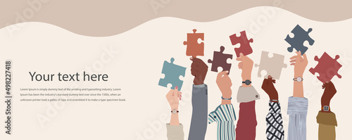Group of multicultural business people with raised arms holding a piece of jigsaw. Colleagues of diverse ethnic groups and cultures. Cooperate - collaborate. Concept of teamwork.Copy space