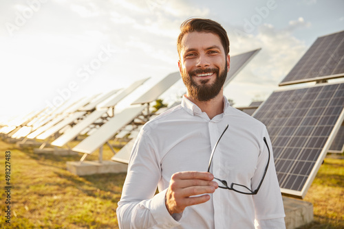 Smiling businessman in white shirt standing on solar power farm