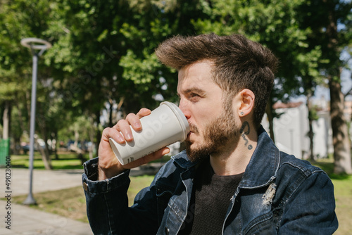 Young man wearing casual clothes drinking coffee. He is looking away while drinking coffee.