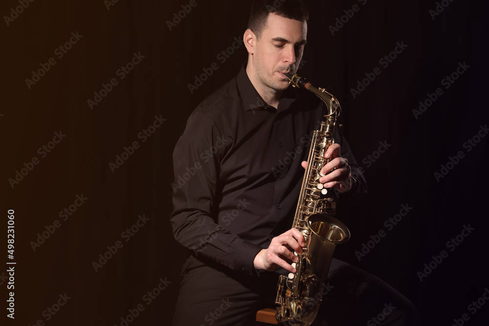 Naklejka premium Young man playing saxophone on dark background. Space for text