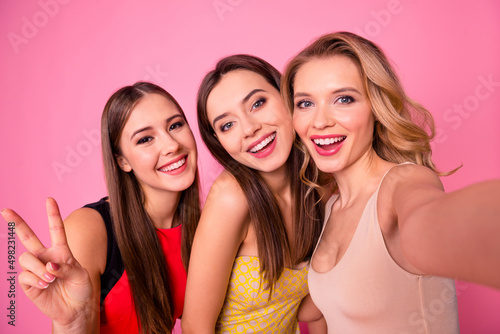 Portrait of gorgeous positive ladies take selfie hand demonstrate v-sign isolated on pink color background