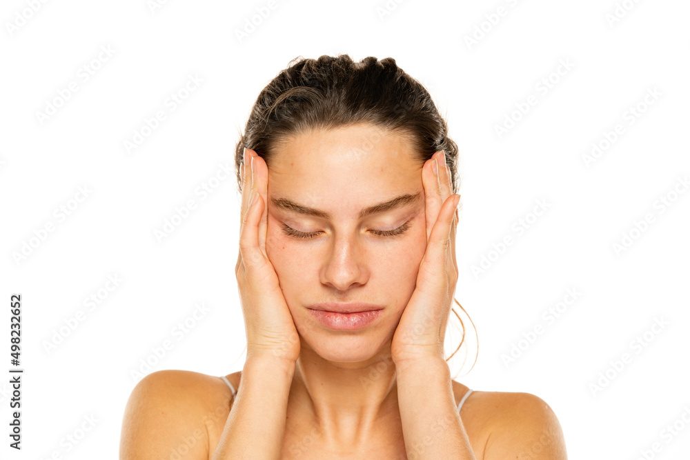 Young woman tightening her face skin with her palms on a white background Young woman tightening her face skin with her palms on a white background