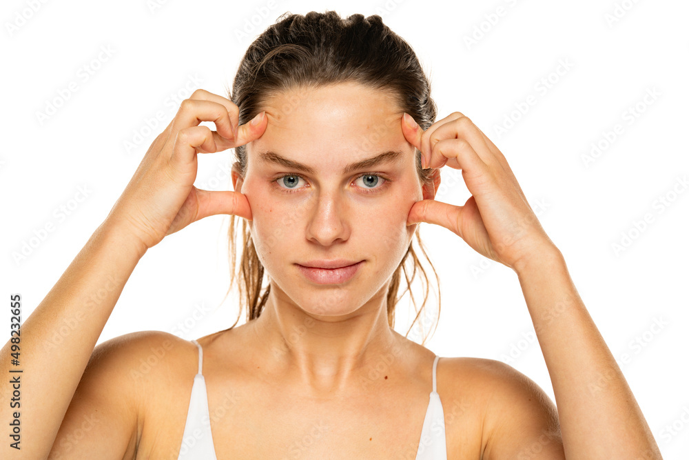 Young woman tightening her face skin with her fingers on a white background