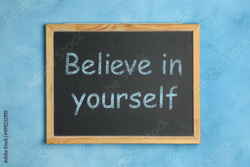 Small chalkboard with motivational quote Believe in yourself on light blue background, top view © New Africa