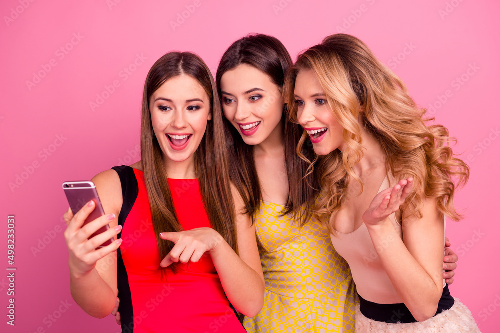 Portrait of three positive excited ladies embrace look telephone isolated on pink color background