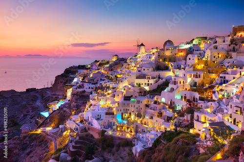 Oia village, Santorini, Greece. View of traditional houses in Santorini. Small narrow streets and rooftops of houses, churches and hotels. Landscape during sunset.