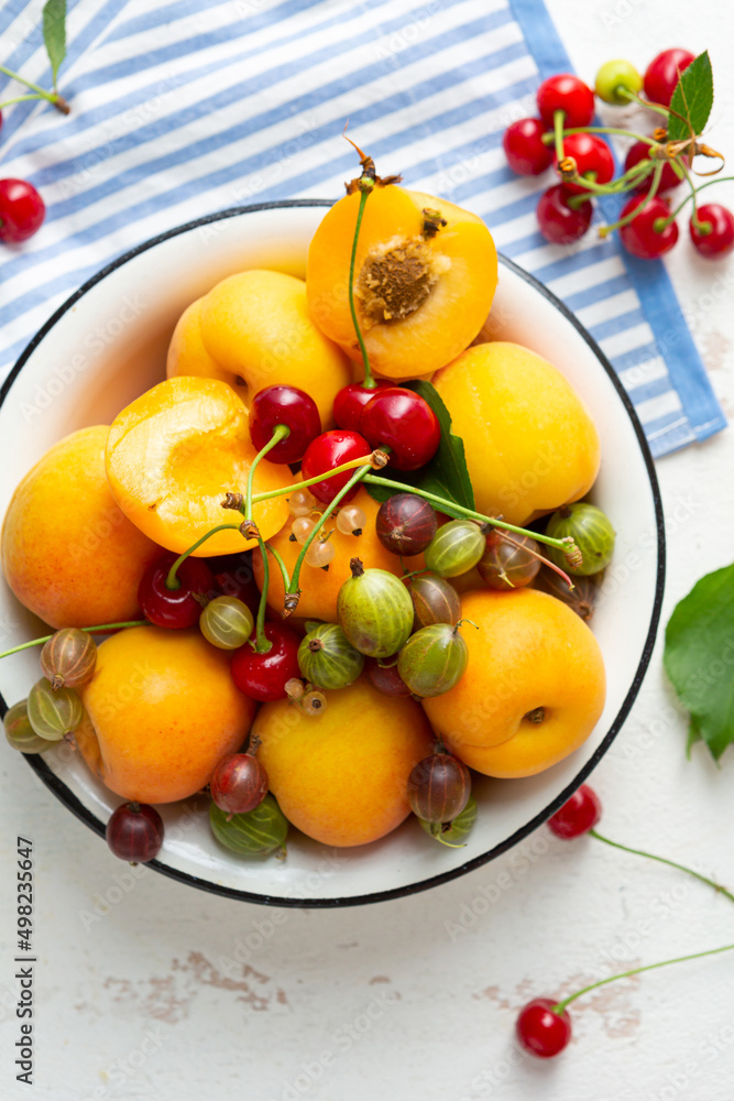 Overhead view of summer fruits cherry and apricot in bowl on white surface