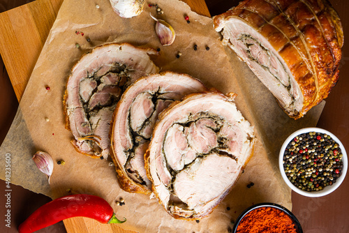 Porchetta on wooden board with chili pepper, garlic and paprika