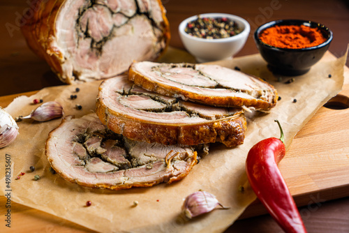 Porchetta on wooden board with chili pepper, garlic and paprika