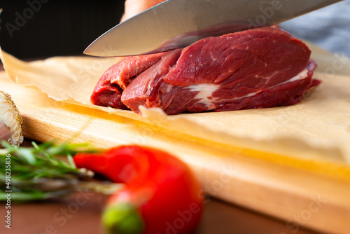 Hand cutting piece of meat with a knife on a wooden board and spices