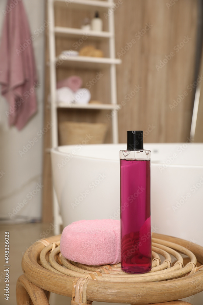 Bottle of shower gel and sponge on wicker table near tub in bathroom, space for text Bottle of shower gel and sponge on wicker table near tub in bathroom, space for text