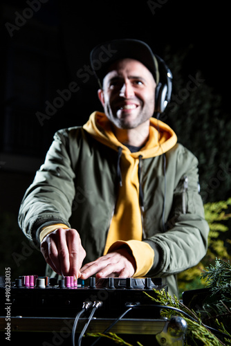 manos DJ vertical chico pincha musica con una mesa de mezclas en una fiesta en bosque vestido con una chaqueta verde, una sudadera con capucha y una gorra, rave party