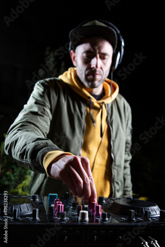 manos DJ vertical chico pincha musica con una mesa de mezclas en una fiesta en bosque vestido con una chaqueta verde, una sudadera con capucha y una gorra, rave party