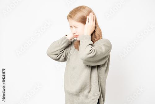 白背景の前で、耳を手で塞いでいる若い女性