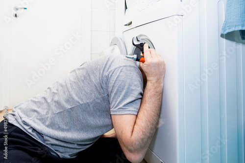 Caucasian man repairing a washing machine, stuck his head in the washing machine.