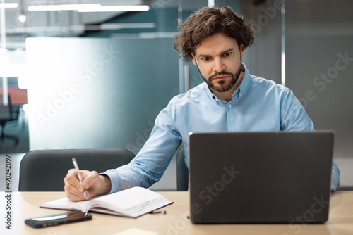 Portrait of focused man using laptop and writing