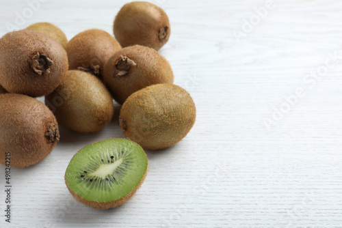 Cut and whole fresh kiwis on white wooden table, space for text