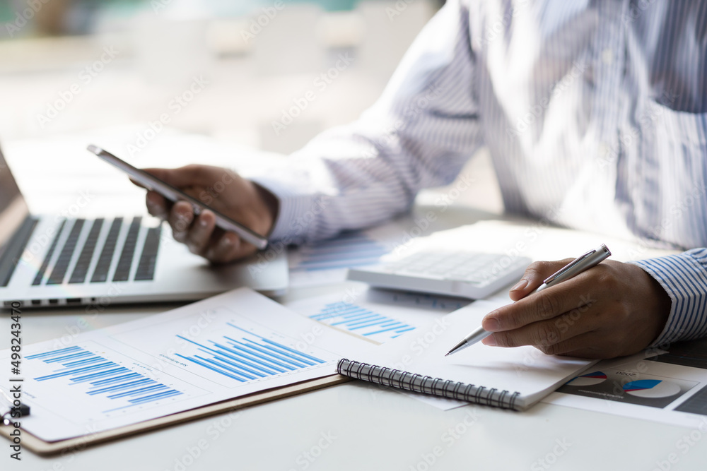 Fototapeta premium Bookkeeper is recording the company's financial growth statistics using graphs as a reference for reviewing and analyzing the results on mobile, Taking notes and analyzing data.