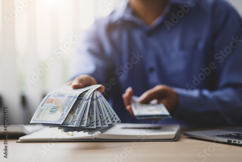 Wealthy businessman counting money and holding cash on his desk is offering you his paycheck Fototapet