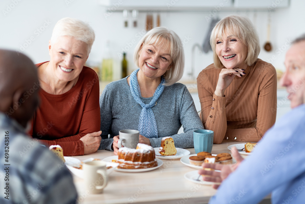 Group of happy senior friends drinking tea with cake together
