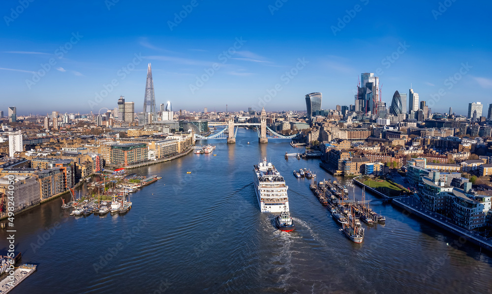 Aerial view of the moder skyline of London with the lifted Tower Bridge and a cruise ship passing under during a sunny morning