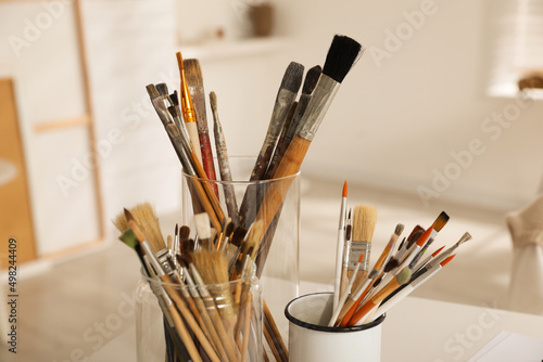 Holders with different paintbrushes on white table in studio, closeup. Artist's workplace