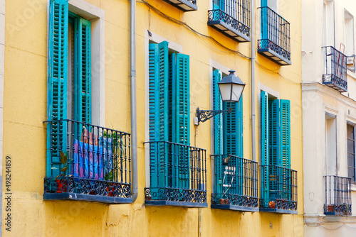 Tiny balconies with vivid blue shutters on vibrant yellow wall. Weathered facades in Lavapies district downtown Madrid, Spain photo