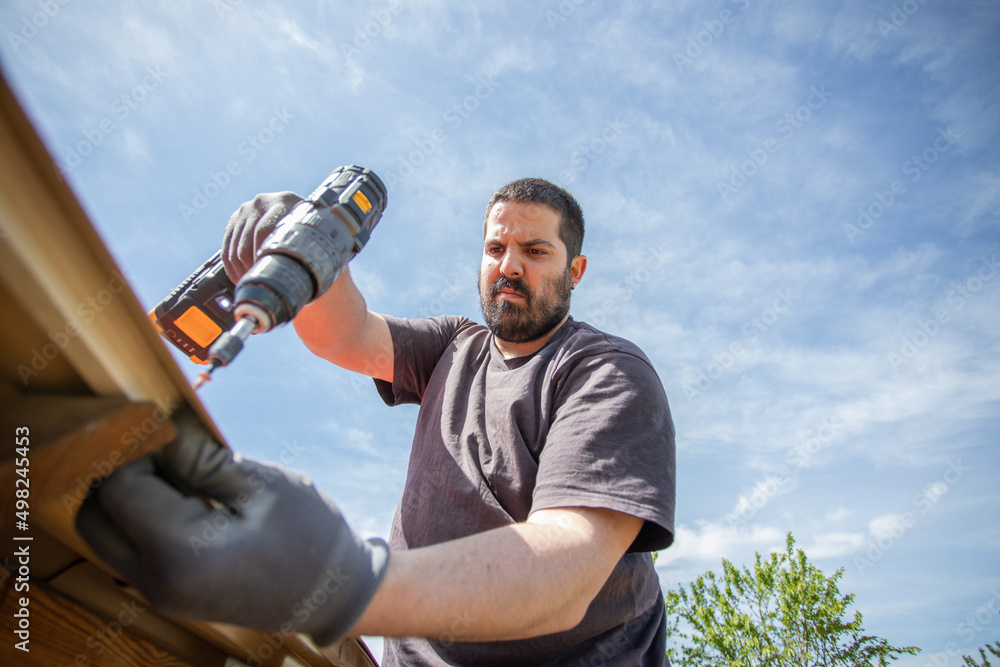 Caucasian man seen from below installing a screw with his electric screwdriver Caucasian man seen from below installing a screw with his electric screwdriver