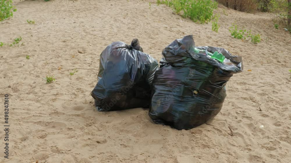 Rubbish, bottles, disposable tableware are collected in large garbage bags on sand near bushes. Disposal of forest or beach trash, litter. Ecological problem, save planet, waste treatment, processing Rubbish, bottles, disposable tableware are collected in large garbage bags on sand near bushes. Disposal of forest or beach trash, litter. Ecological problem, save planet, waste treatment, processing