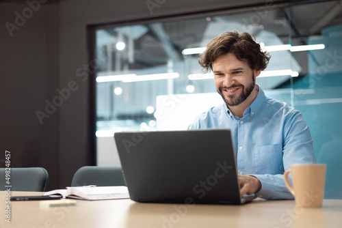 Smiling businessman using laptop sitting at desk in office