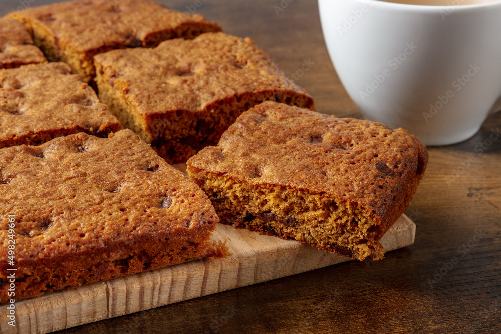 Blondie brownie dessert bars with chocolate chips, a close-up on a dark rustic wooden background with a cup of tea Blondie brownie dessert bars with chocolate chips, a close-up on a dark rustic wooden background with a cup of tea