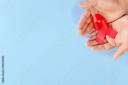Top view of male hand holding red ribbon on blue background. AIDS, HIV, heart disease and stroke awareness concept.	
