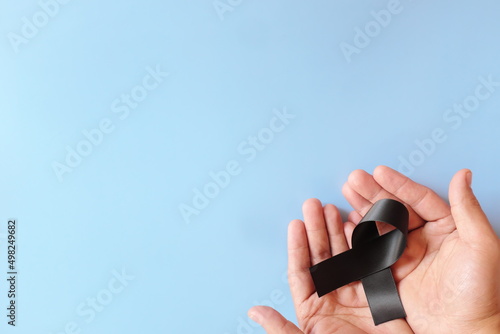 Top view of male hand holding black ribbon in blue background with copy space. Melanoma or skin cancer, gang prevention and narcolepsy awareness concept.