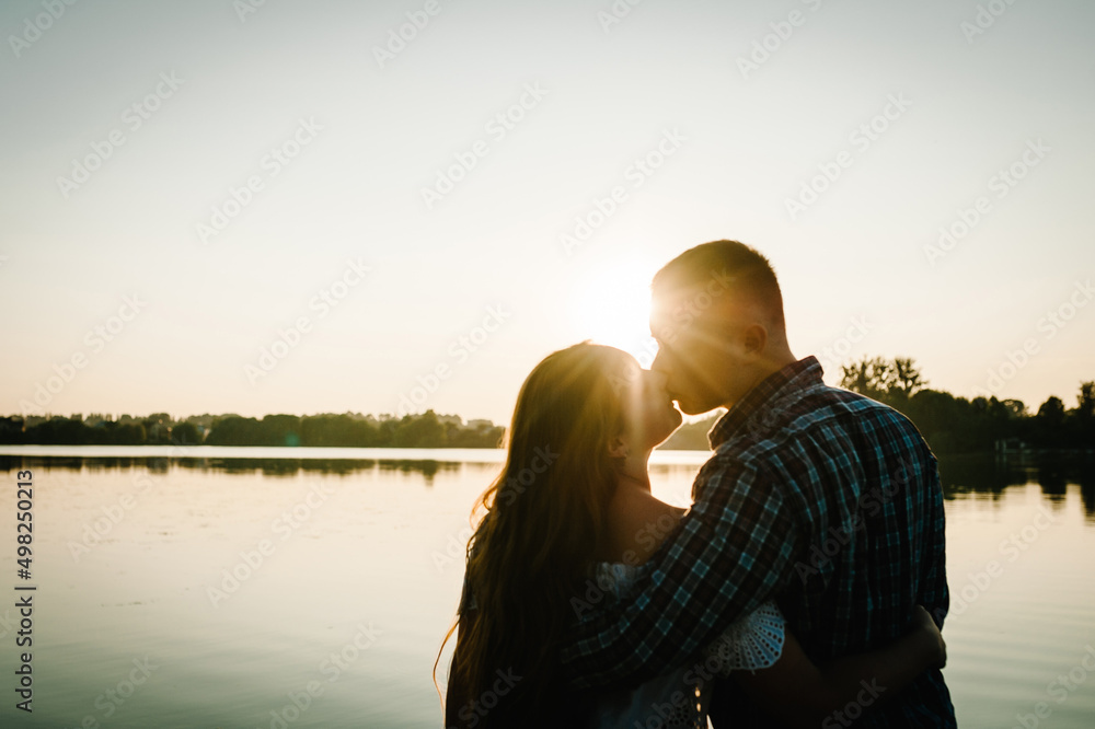 Silhouette of a couple. Young couple kissing and hugging at sunset in spring. A man and woman on background of sun. Concept of love and family. Close Up.
